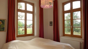 A bedroom with a large bed, two windows with curtains, a hanging lamp, and a radiator.