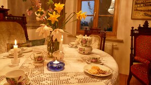 A dining table set with floral-patterned tea sets, a vase with flowers, and candles.