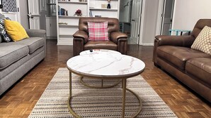 A living room with a brown leather sofa, a grey sofa, a round coffee table, and a white shelving unit with decorative items.