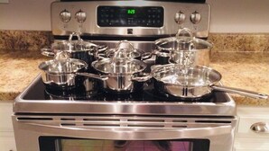 A stainless steel stove with pots and pans on it, a digital clock, and a microwave oven below.