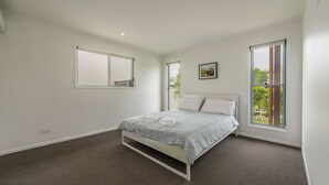 Een slaapkamer met een bed, twee ramen, een foto aan de muur en een vloerbedekking.