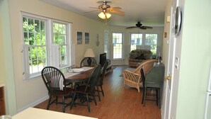 A dining area with a wooden table and chairs, a ceiling fan, and large windows with shutters.