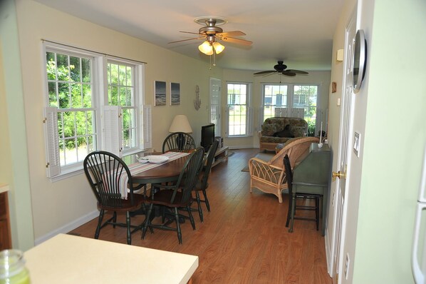 A dining area with a wooden table and chairs, a ceiling fan, and large windows with shutters.