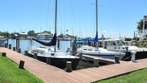 A marina with several boats docked, a wooden walkway, and a clear blue sky.