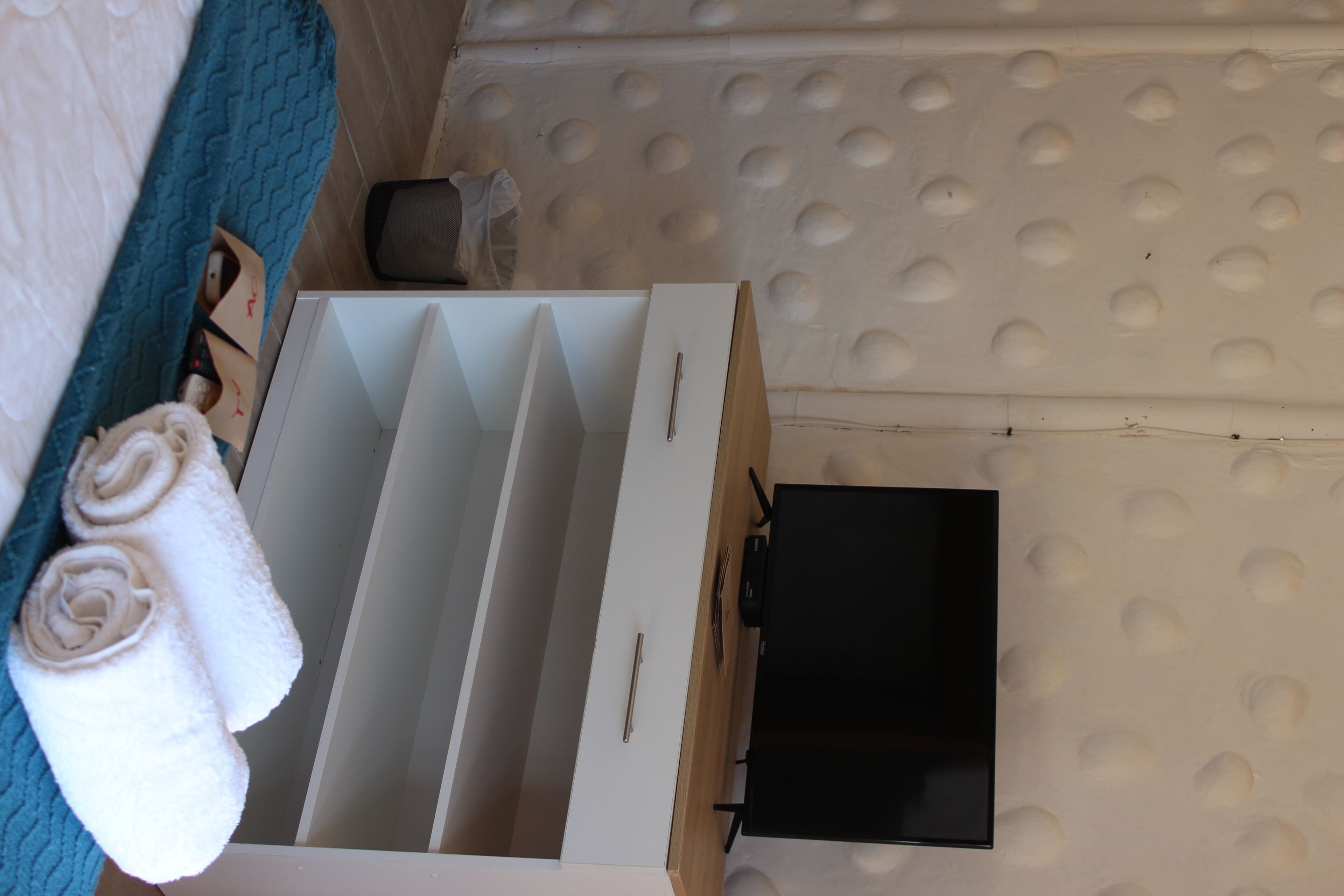 A room with a bed, a white dresser, a black TV, and a blue wall.