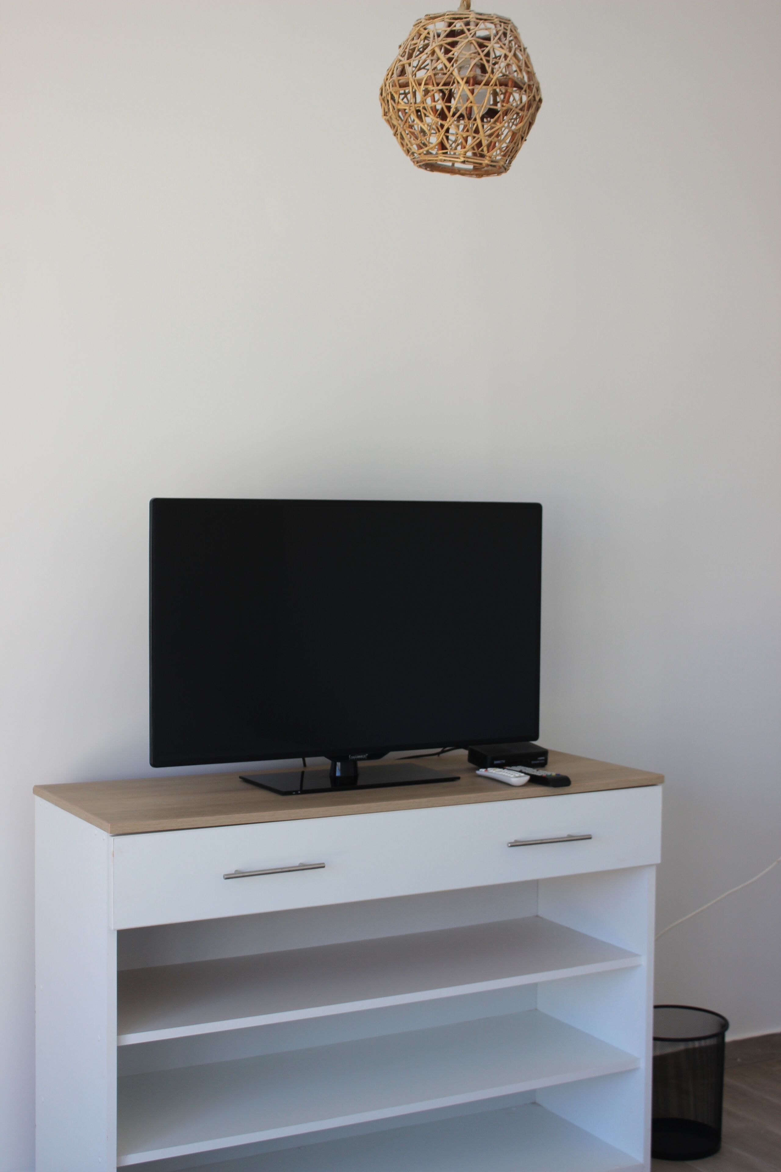 Un mueble blanco para televisor con un televisor de pantalla plana, un control remoto y un objeto negro pequeño encima.