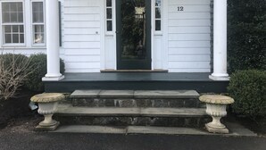 Et hvidt hus med en sort hoveddør, nummer 12, og en lille veranda med trapper og to stentofler.