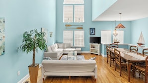 A living room with a sofa, coffee table, dining table with chairs, a potted plant, and a TV.