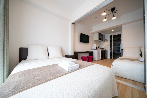 Ein modernes Hotelzimmer mit zwei Betten, einem Flachbildfernseher, einer Küchenzeile und einer Schiebetür zum Badezimmer.