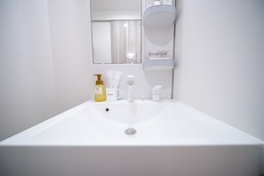 Ein weißes Waschbecken mit Spiegel darüber, einer Seifenspender und eine Zahnbürstenhalterung.