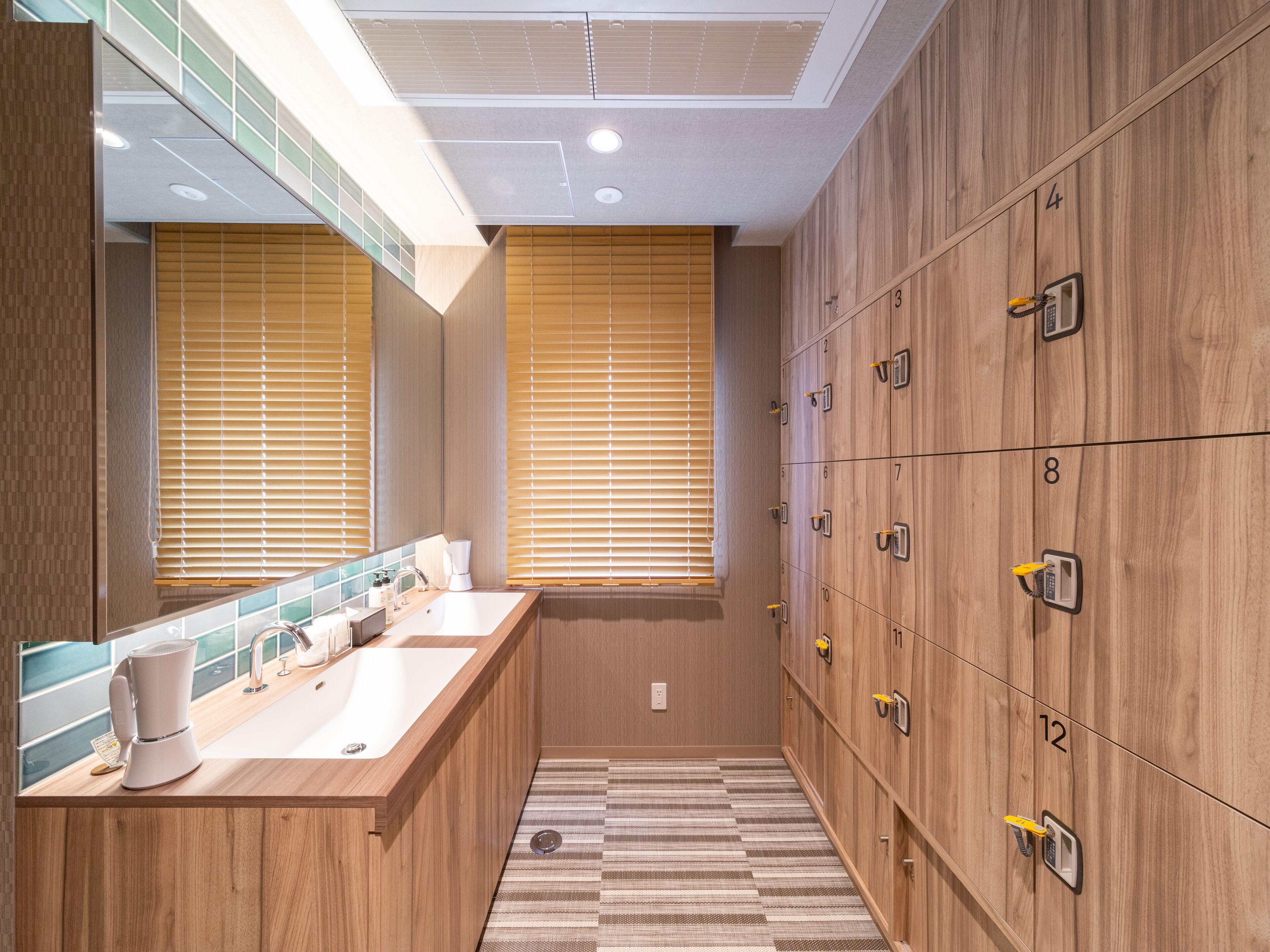 A modern bathroom with wooden lockers, a sink with a mirror, and a striped floor.