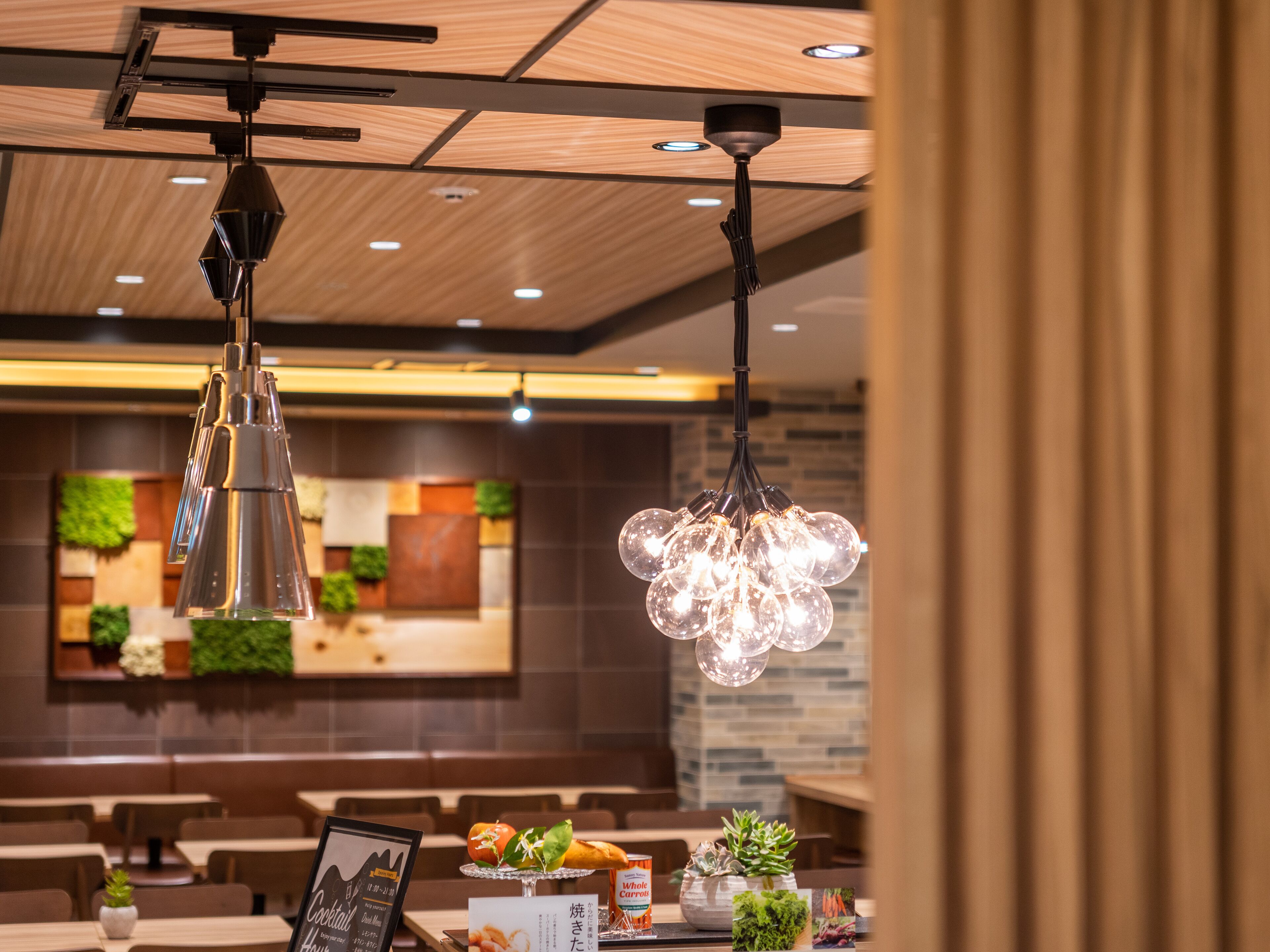 A restaurant interior with hanging pendant lights, wooden ceiling, and a menu stand with food items.