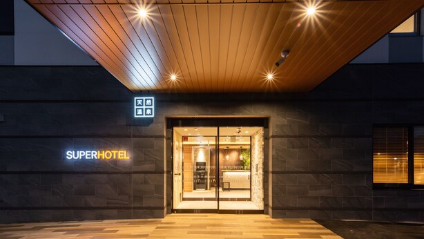 Das Äußere eines Hotels im modernen Stil, mit einer Holzbalkendecke und einem Schild mit der Aufschrift 'SUPERHOTEL'.