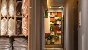 Ein Flur mit einem Holzregal, das gefaltete Leinentücher zeigt, einer Wand mit vertikalem Garten und einem gefliesten Boden.