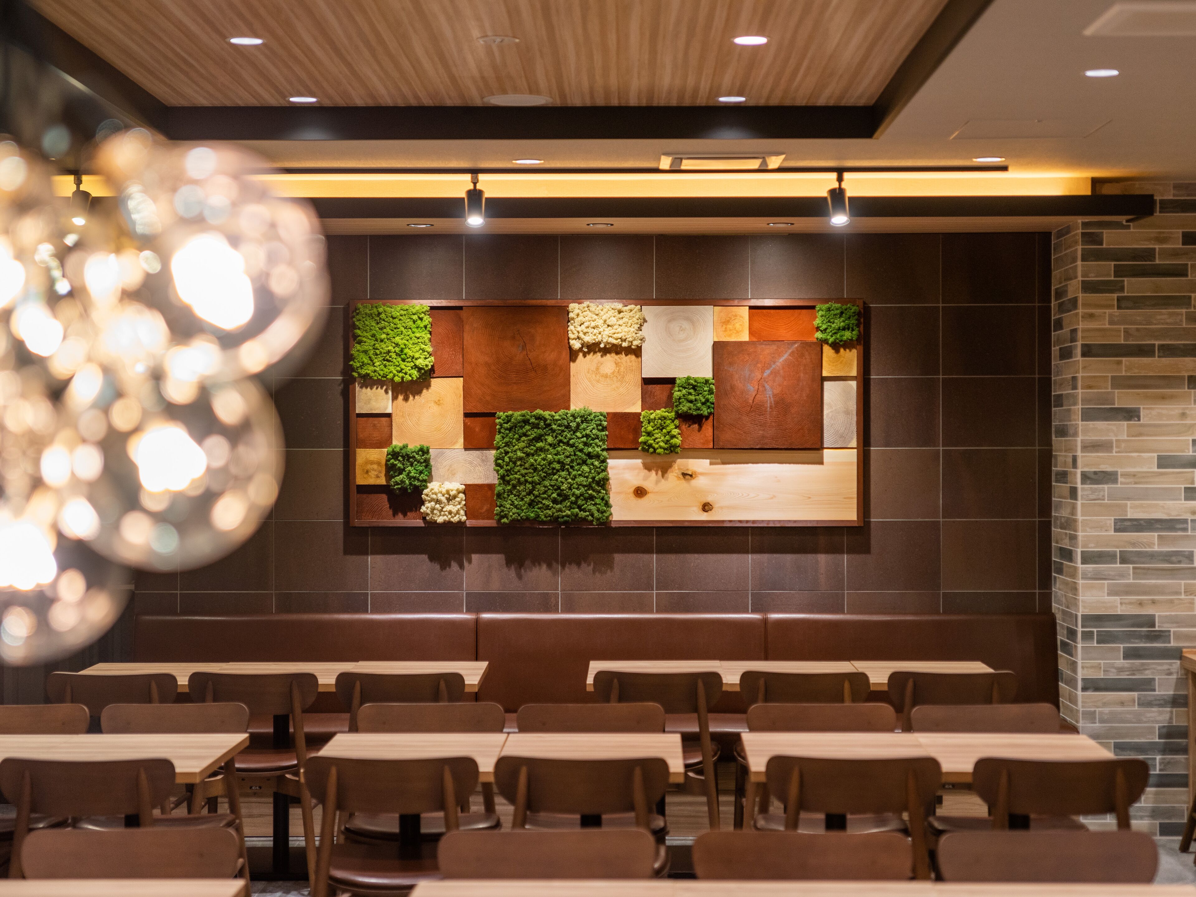 Ein Restaurantinneres mit modernem Design, das eine lange Theke, Sitzgelegenheiten in Form von Boxen und eine wandmontierte Dekoration sowie eingelassene Beleuchtung zeigt.