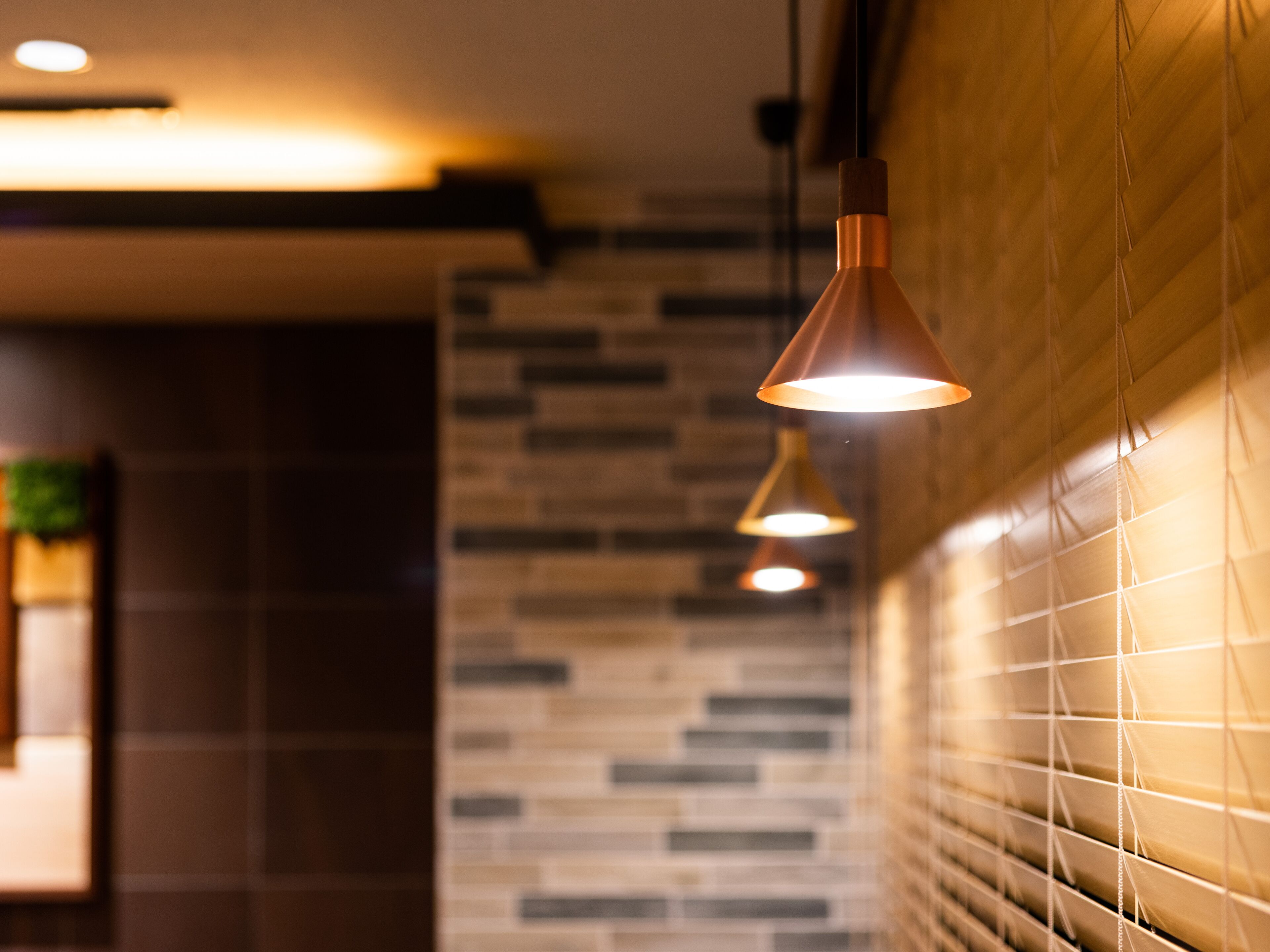 A modern interior with pendant lighting, a tiled wall, and a wooden slat design.