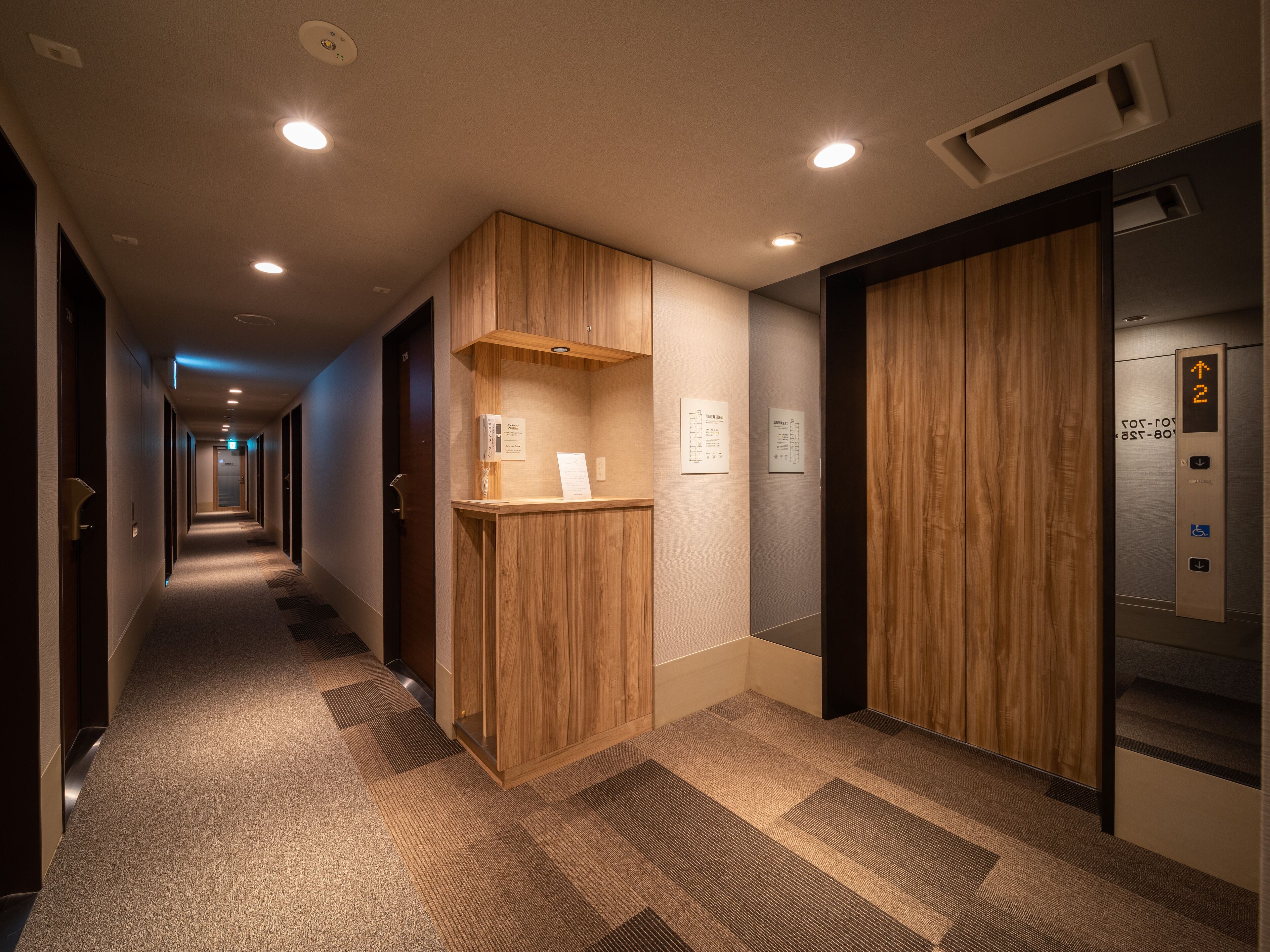 A hotel hallway with a reception desk, an elevator, and a carpeted floor.