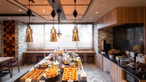 Ein reichhaltiges Frühstücksbuffet mit verschiedenen Backwaren und Speisen, Holzdetails und Pendelleuchten.