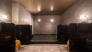 A sauna room with two wooden benches, a tiled floor, and a brick wall with two wall-mounted lights.