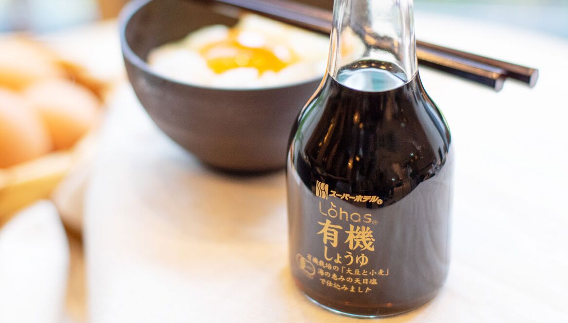 Una botella de salsa de soja con texto japonés y un plato de arroz con palillos.