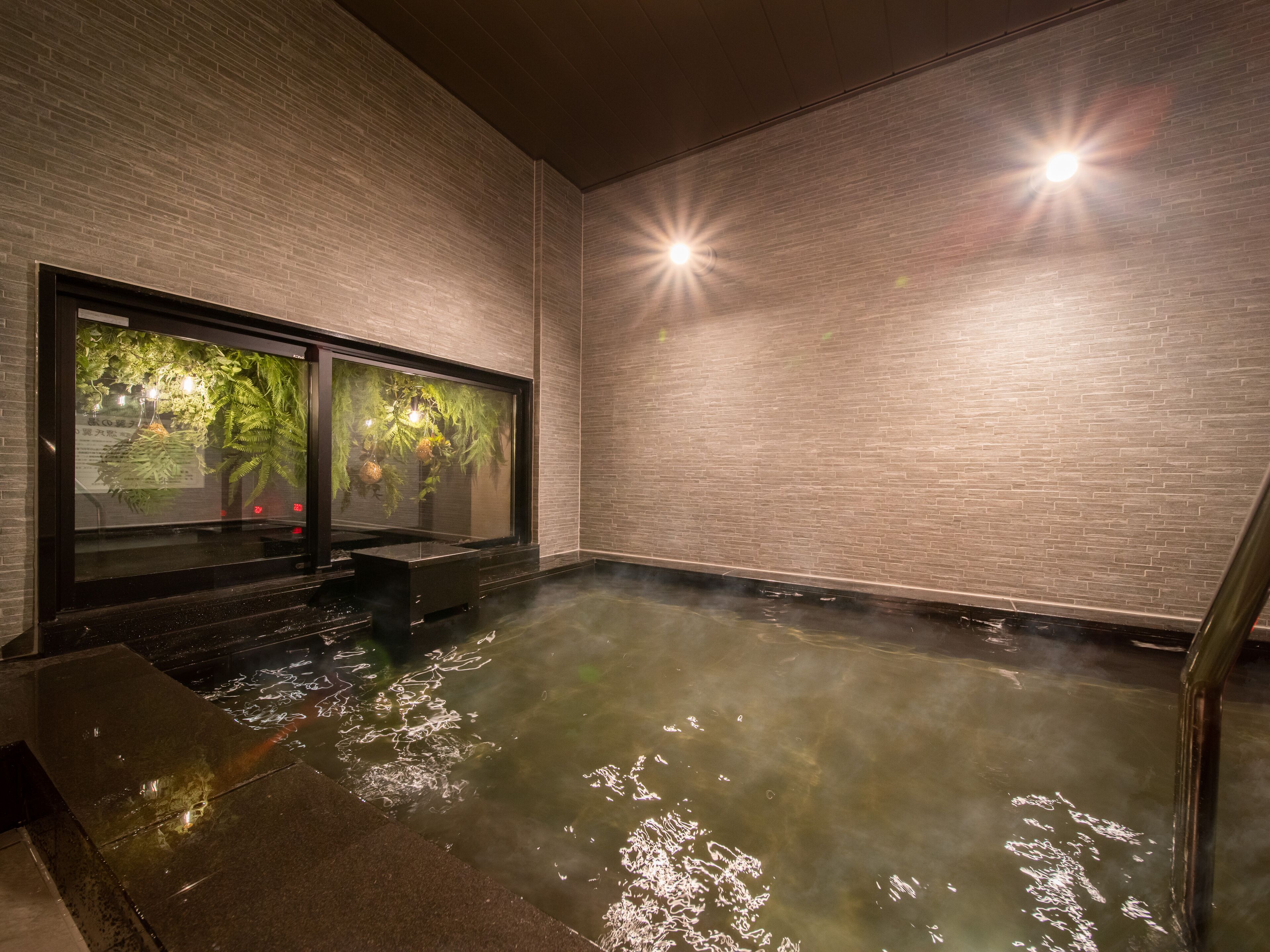 A hot spring area with a glass enclosure, tiled floor, and brick walls.
