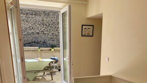 A bedroom with a bed, a view through an open door to an outdoor area, and a framed picture on the wall.