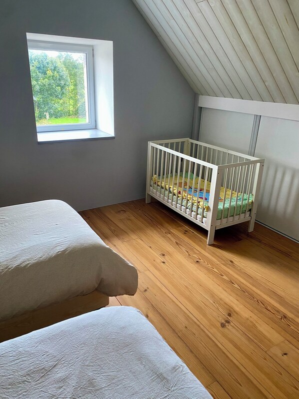 A room with a crib, two beds, a window, and a sloped ceiling. - A charming guesthouse, ideal for families. (Saint-Euphrône)