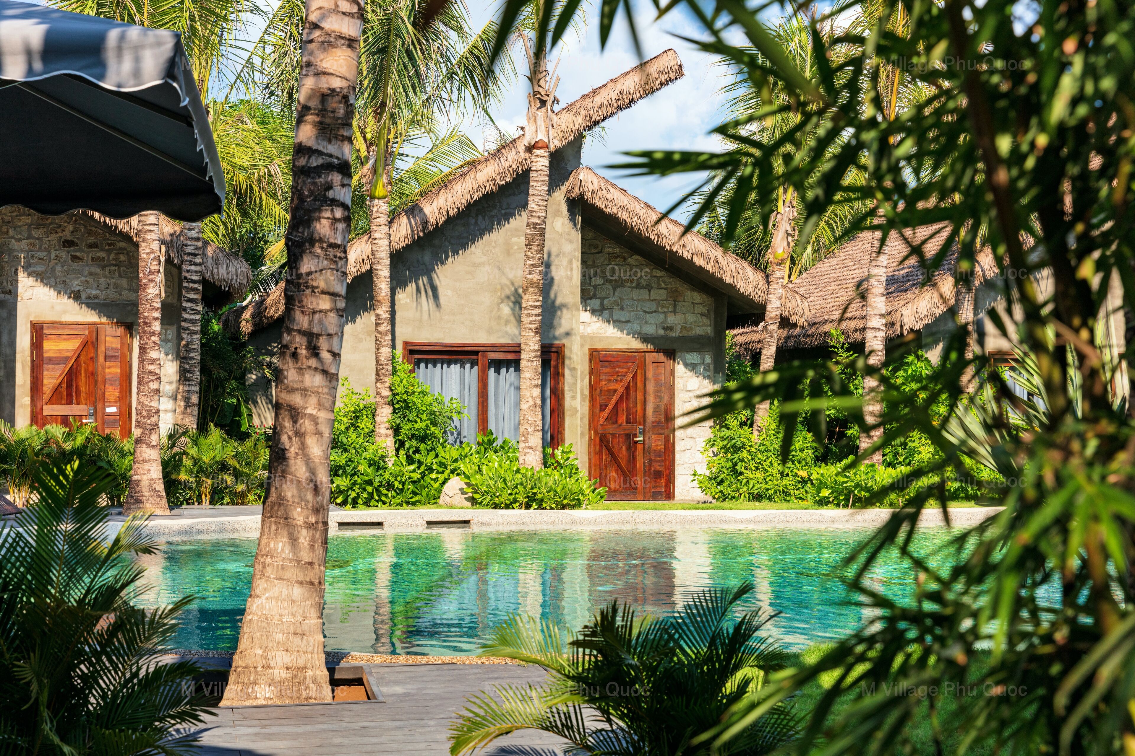 A pool area with a stone building, palm trees, and a thatched-roof structure.