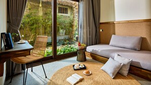 A cozy room with a sofa, a wicker chair, a dining table with a bowl of fruit, a tray with a teapot and a cup, and a book on the floor. - M Village Phu Quoc (Phu Quoc)