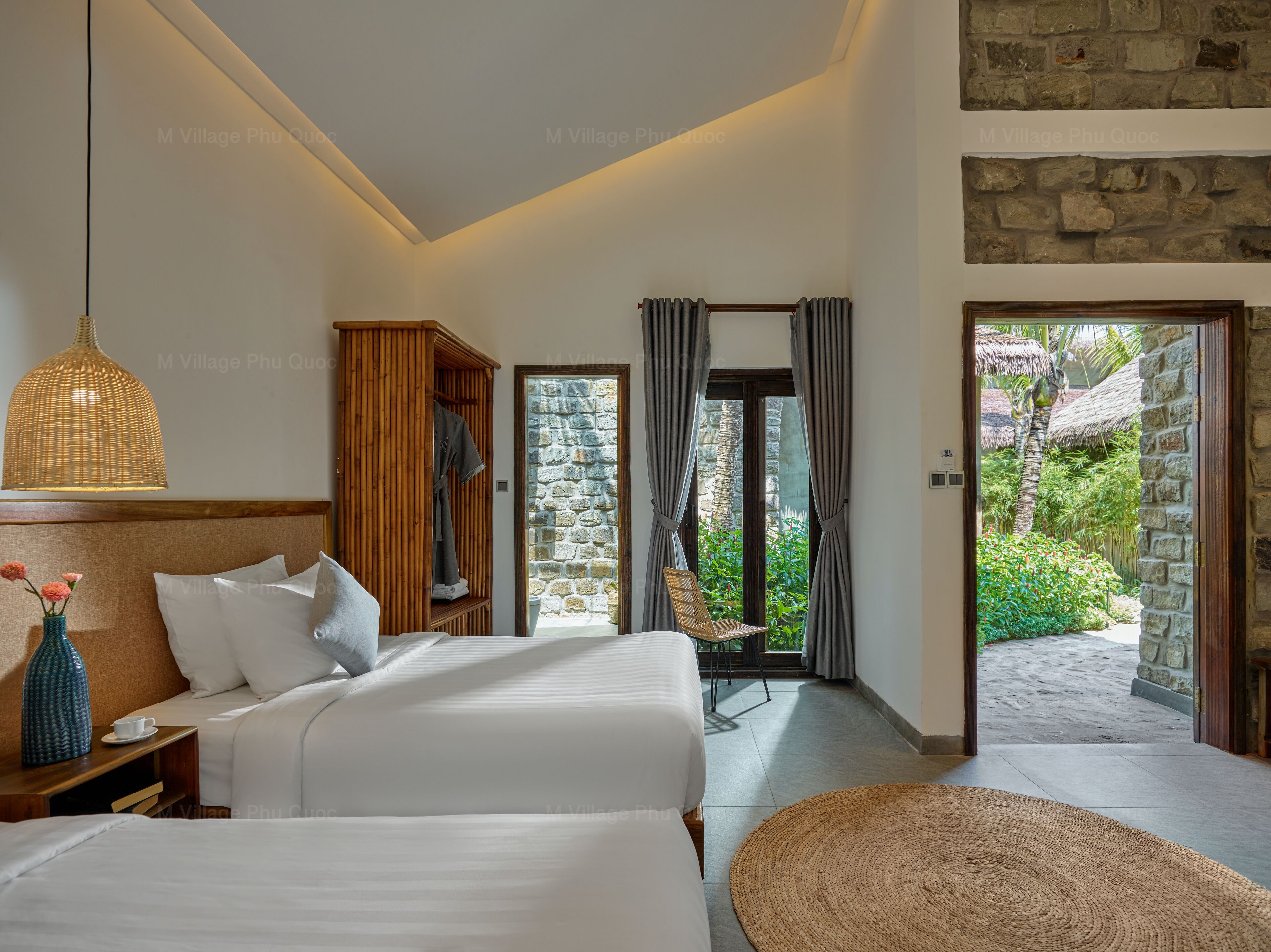 A hotel room with a bed, a wardrobe, a nightstand, a lamp, and a view of the garden through a glass door.