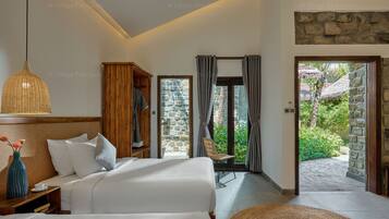 A hotel room with a bed, a wardrobe, a nightstand, a lamp, and a view of the garden through a glass door.