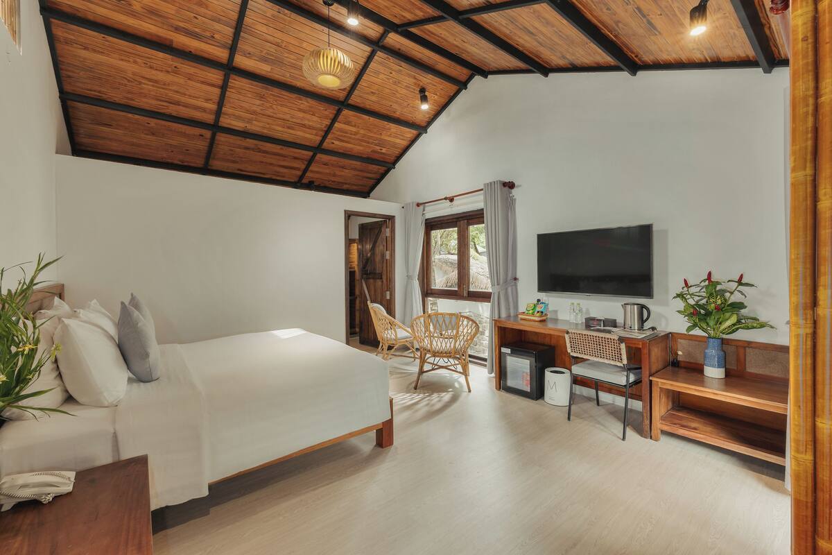 A bedroom with a bed, a desk, a chair, a TV, and a plant.