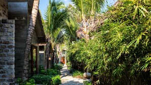 A stone building with a narrow pathway surrounded by lush greenery and palm trees. - M Village Phu Quoc (Phu Quoc)
