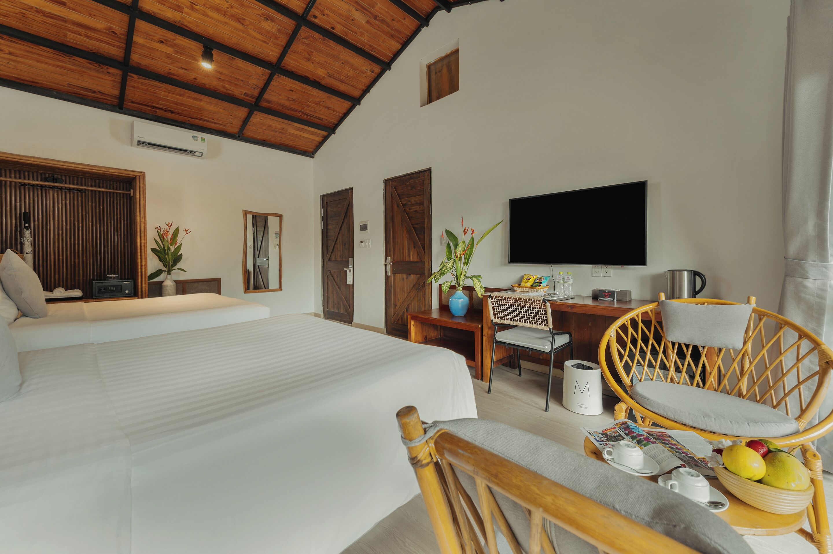 Amplia habitación con una cama grande, techo de madera, televisor, mesa de comedor con sillas y una pequeña cocina.