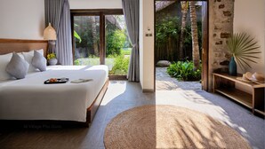 A bedroom with a large bed, a bedside table with a lamp, and a view of a garden through a glass door. - M Village Phu Quoc (Phu Quoc)