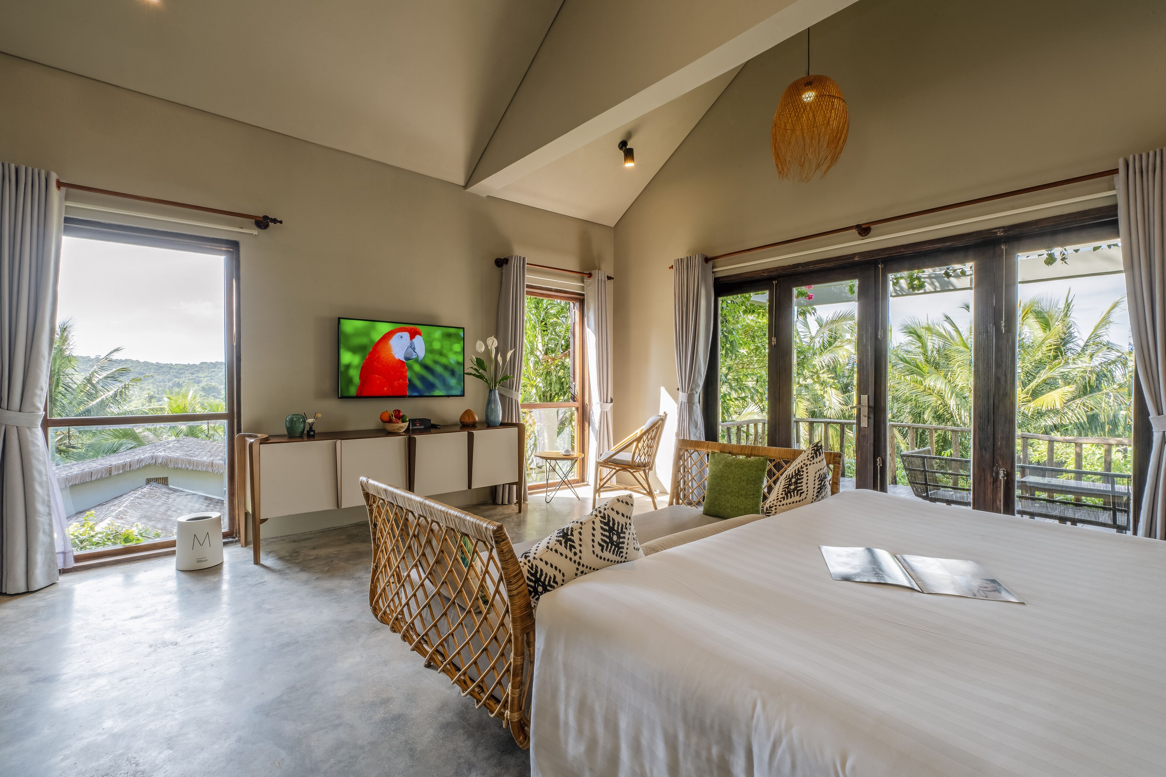 A spacious bedroom with a large bed, a television, and a balcony with a view of palm trees.