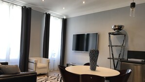 A modern living room with a round table, dark chairs, a white sofa, a black TV, and a decorative vase. - CANNES APPART. LUXURY 50 m2 HYPER CENTER (Cannes)