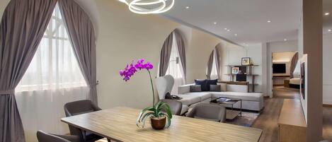 A modern hotel room with a dining area, a sofa set, and a television.