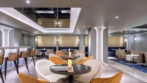 A modern hotel lobby with round tables, comfortable seating, and a skylight ceiling. - Mercure Jakarta Batavia (Jakarta)