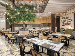 Um restaurante com várias mesas, cadeiras e uma grande árvore como peça central.