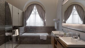 A modern bathroom with a bathtub, two sinks, a large mirror, and a glass shower enclosure. - Mercure Jakarta Batavia (Jakarta)