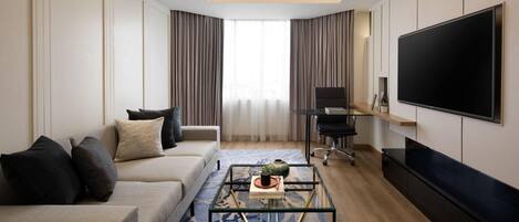Una sala de estar moderna con un sofá, una mesa de centro, televisor y un amplio ventanal con cortinas.