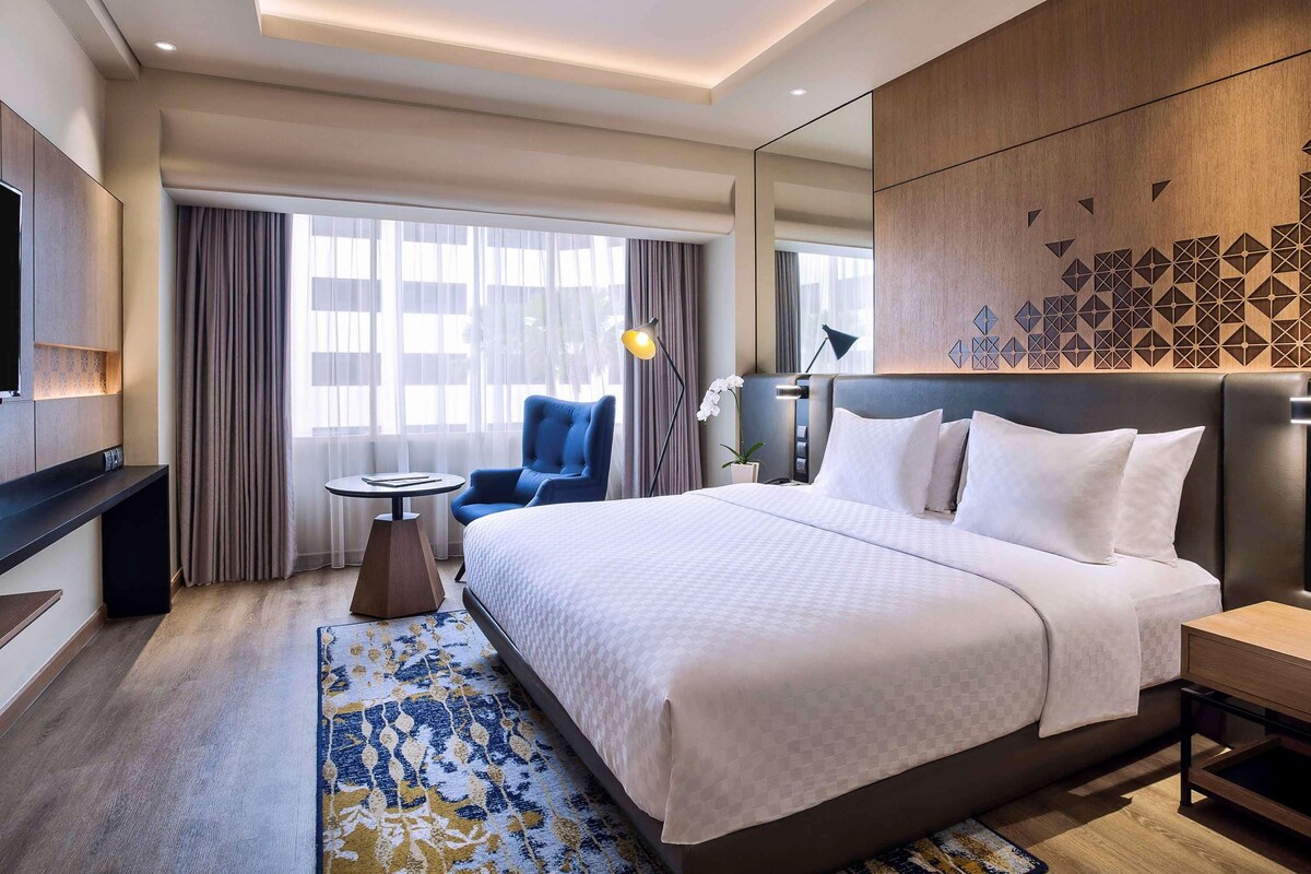 Habitación de hotel con una cama grande, un escritorio, una silla, un televisor y una ventana con cortinas.
