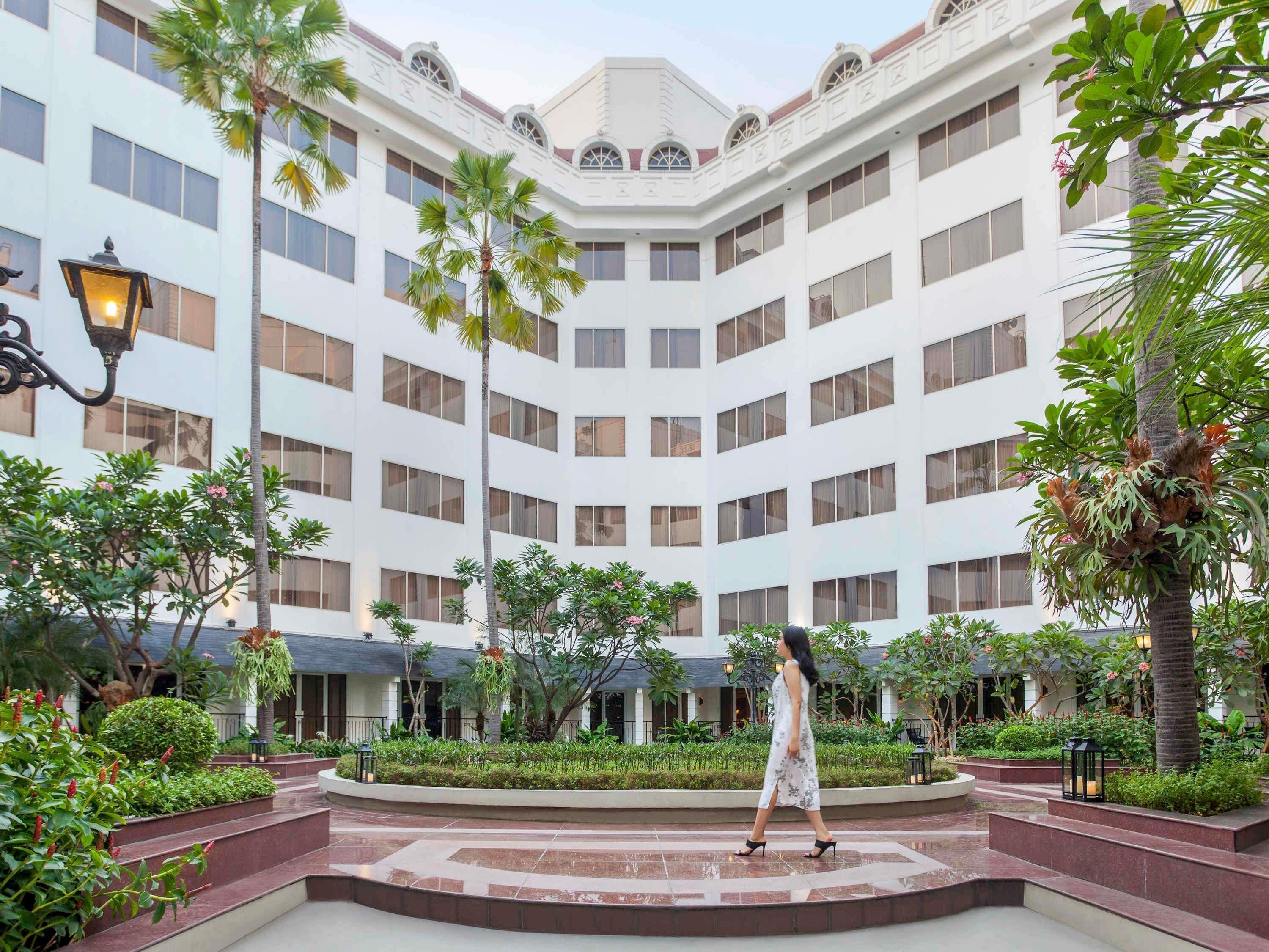 A hotel courtyard with a central circular area, palm trees, and a building with multiple windows.