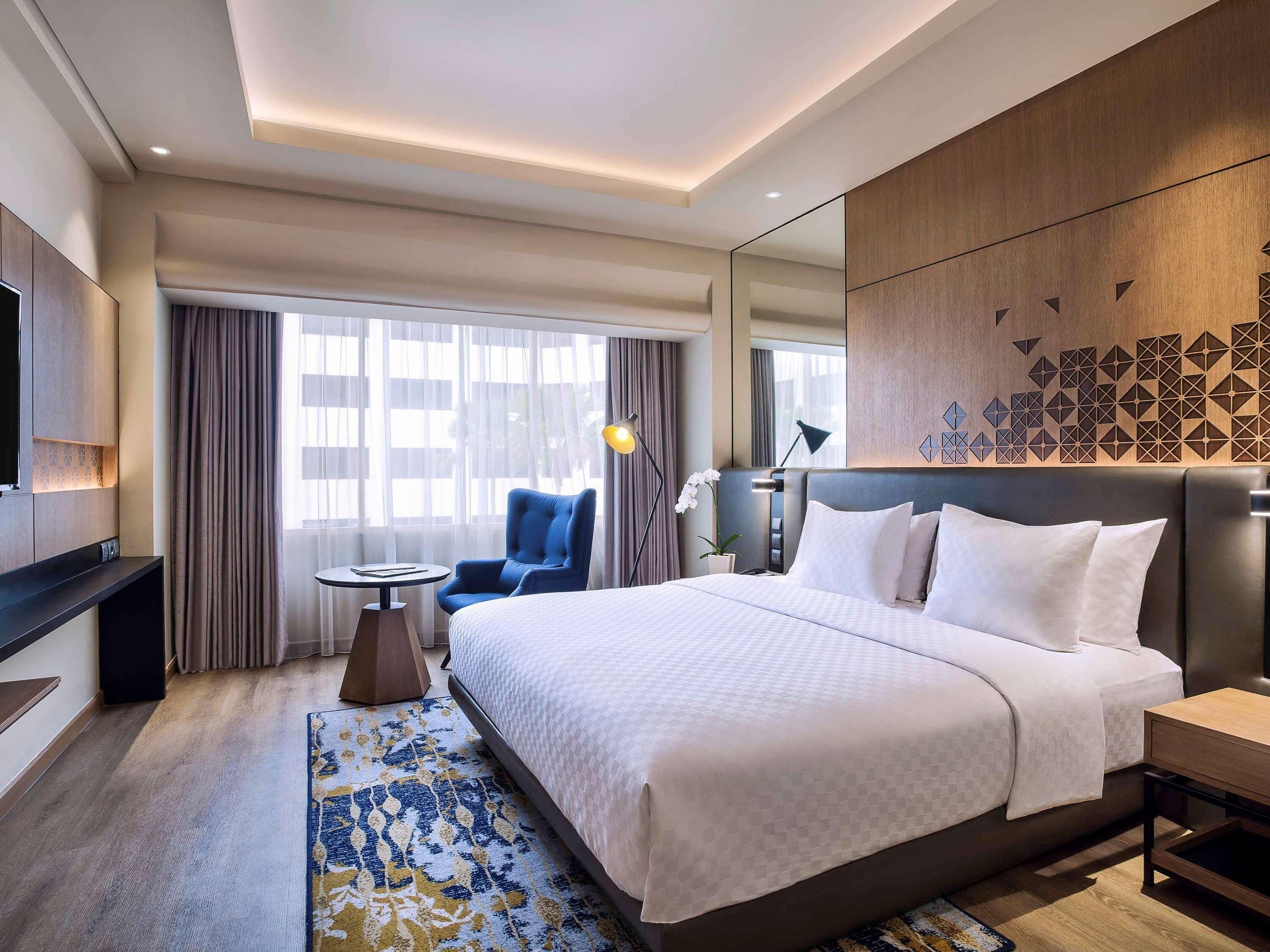 A hotel room with a large bed, a desk, a chair, a TV, and a window with curtains.