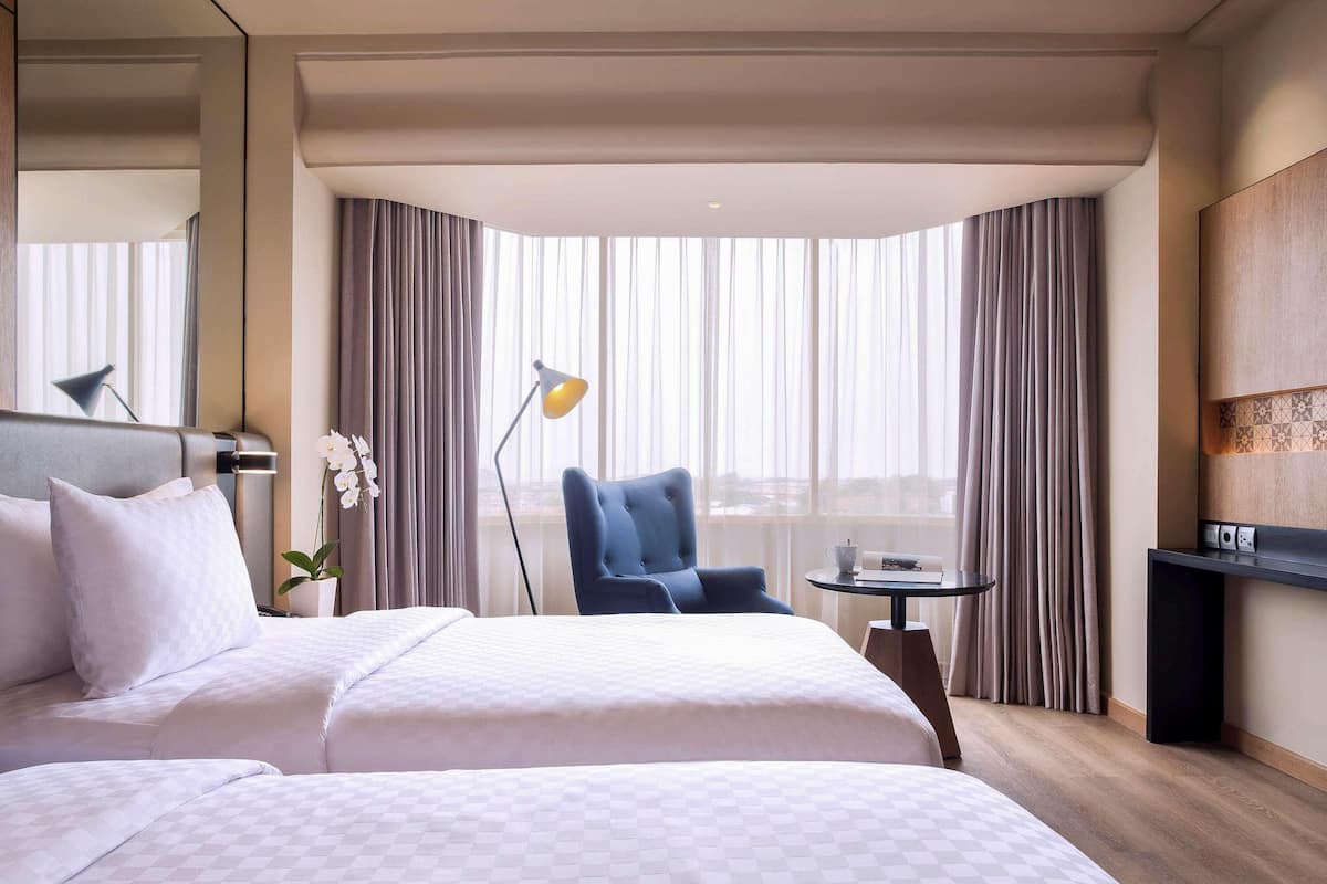 A hotel room with a large bed, a desk, a chair, a lamp, and a view through the window.