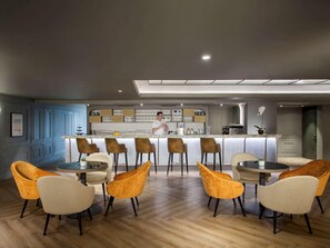 A modern bar area with a bartender, wooden bar counter, and seating with bar stools and round tables. - Mercure Jakarta Batavia (Jakarta)