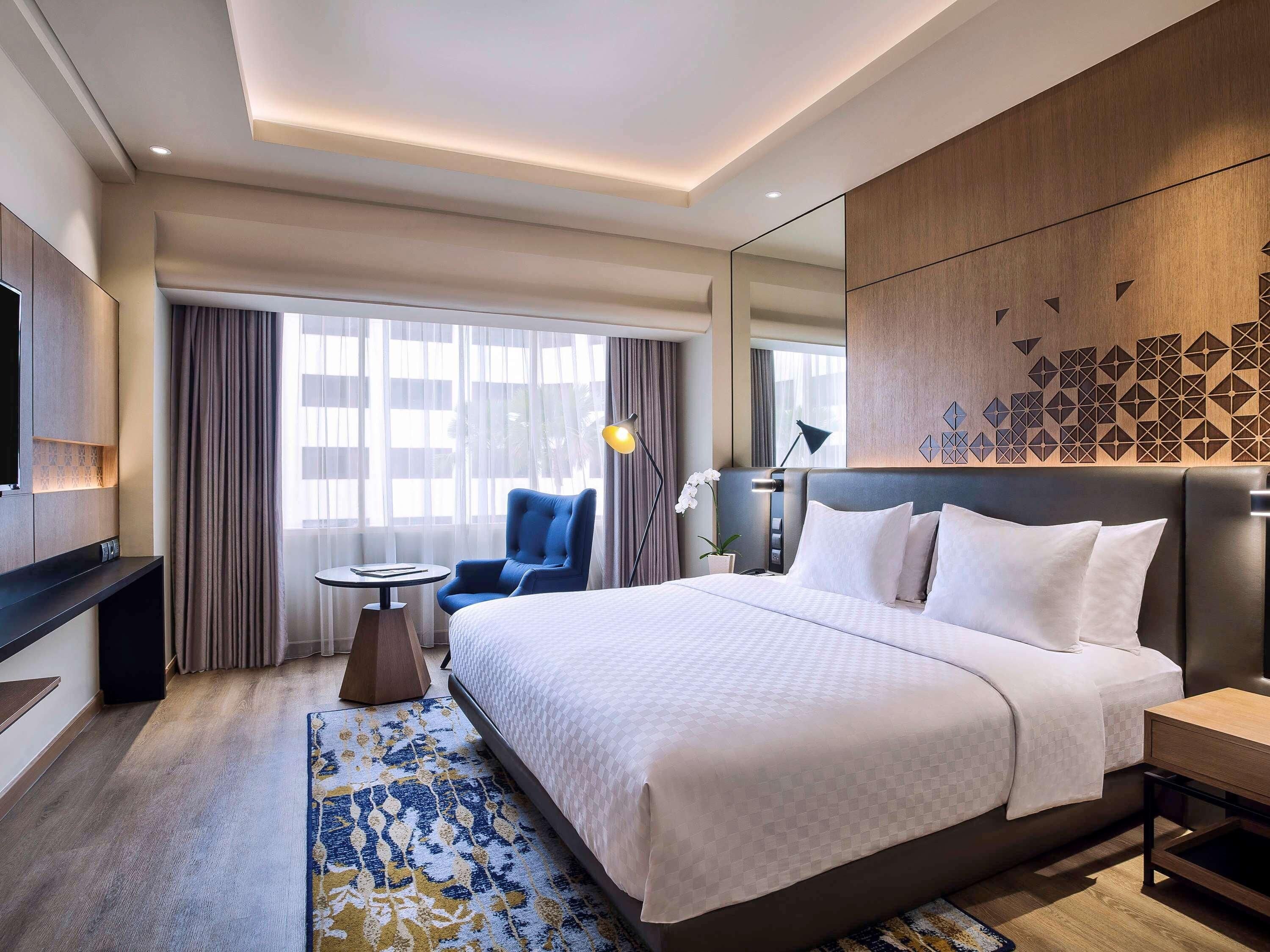 Habitación de hotel con una cama grande, un escritorio, una silla, un televisor y una ventana con cortinas.