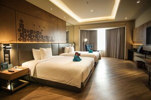 Quarto de hotel com duas camas, uma escrivaninha, uma cadeira, uma televisão e uma janela grande com cortinas.