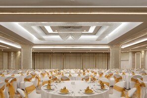 A banquet hall with round tables, white chairs with gold sashes, and a central chandelier. - Mercure Jakarta Batavia (Jakarta)